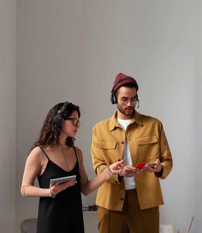 Man and woman wearing wireless headphones, using tablet and smartphone, modern casual style indoors